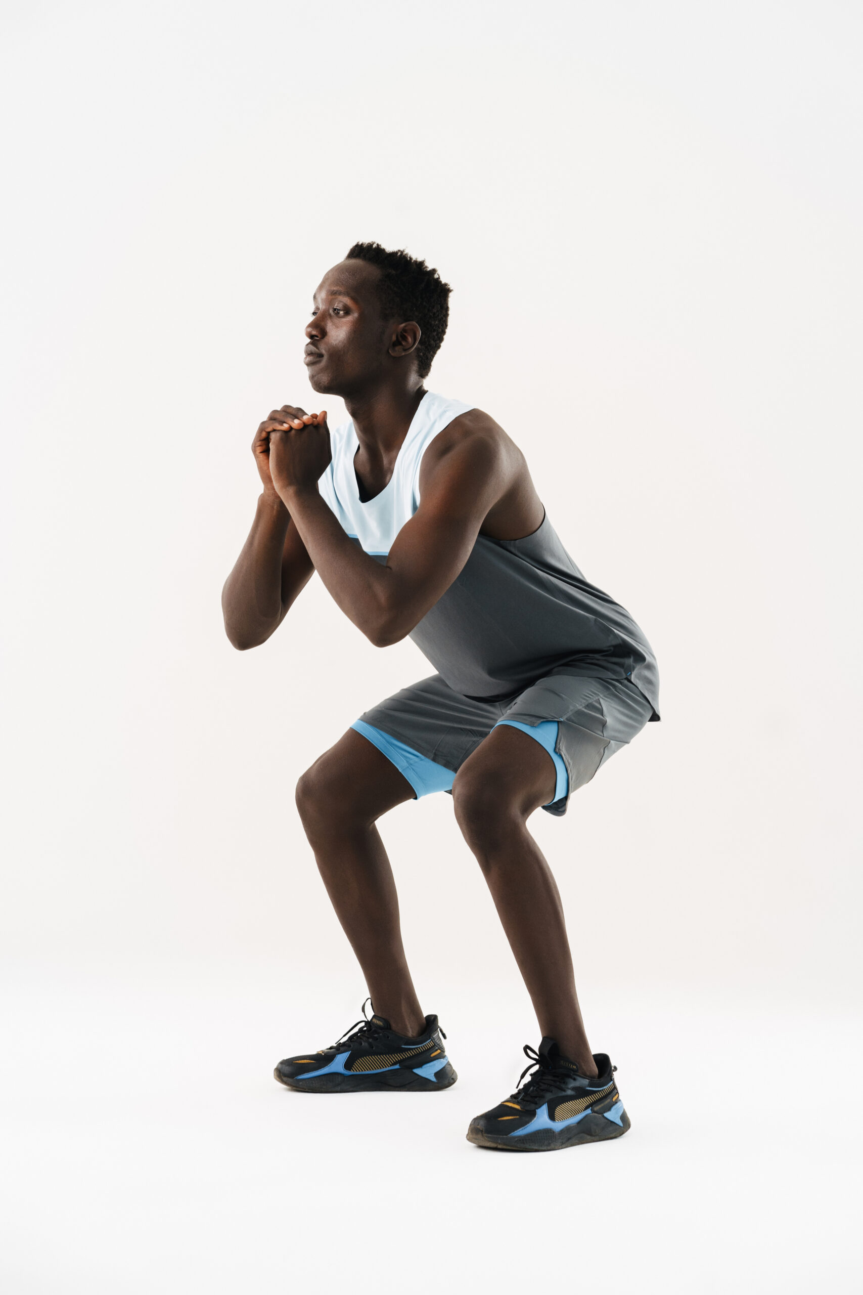 A man in athletic wear is performing a squat exercise, with his hands clasped together in front of him. He stands on a plain white background, possibly demonstrating techniques for Pelvic Floor Therapy in Orlando, FL.