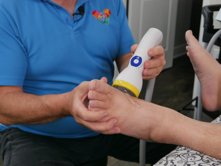 A person applies a handheld medical device to the foot of another person in a clinical setting, demonstrating how shockwave therapy can be used to address conditions related to sexual health or pelvic pain.