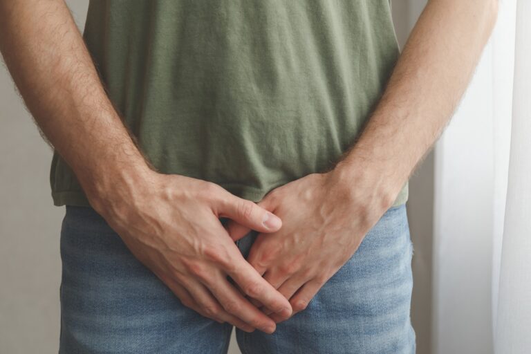 A person wearing a green shirt and blue jeans stands with their hands covering their groin area, perhaps mindful of pelvic health as they consider simple goals for a New Year reset.