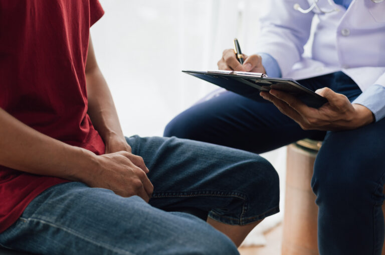 A person in casual clothes sits across from a healthcare professional taking notes on a clipboard during a consultation about common pelvic symptoms.